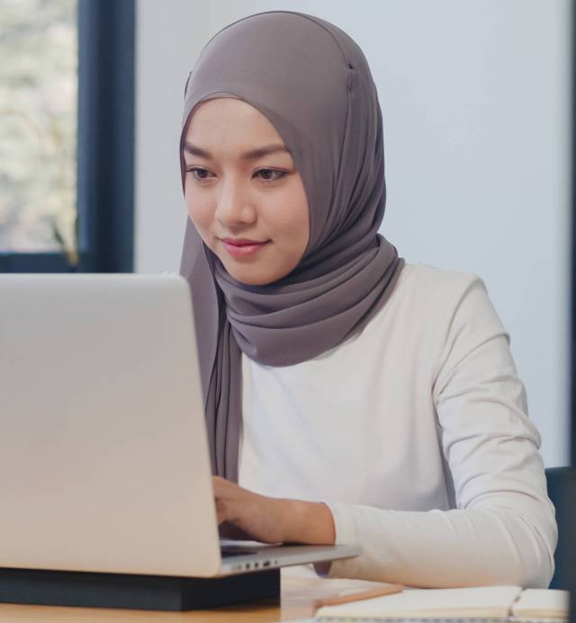 Beautiful Asia muslim lady casual wear working using laptop in modern new normal office. Working from home, remotely work, self isolation, social distancing, quarantine for coronavirus prevention.